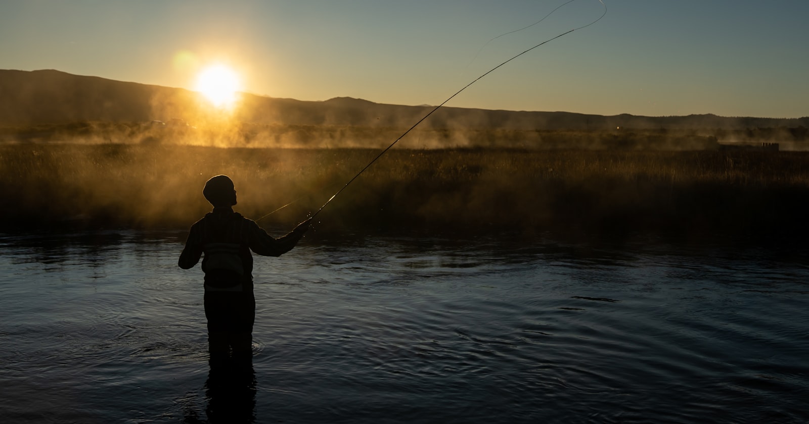 Angler casting on a lake at sunset